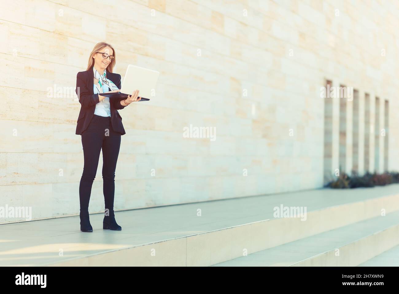 Young business woman working on laptop outside office, success concept Stock Photo