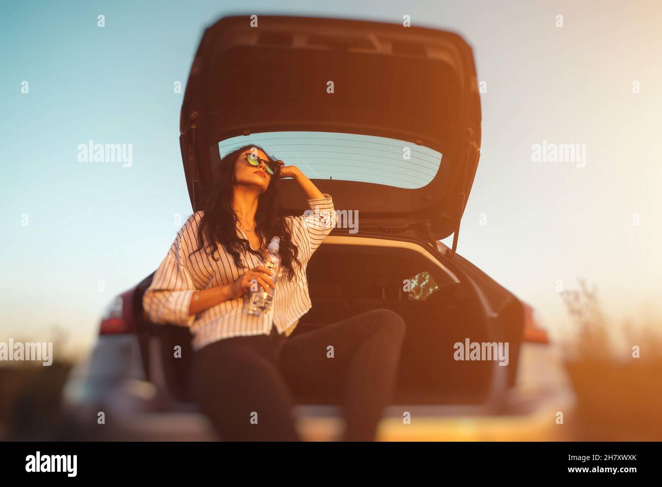 Carefree young woman enjoying sunlight in he boot of her car, youth and travel lifestyle concept Stock Photo