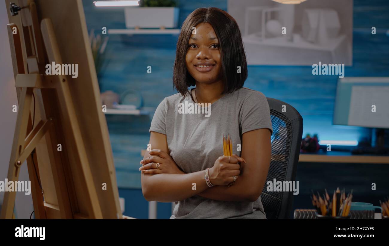Smiling black artist sitting in art studio space with craft tools and ...