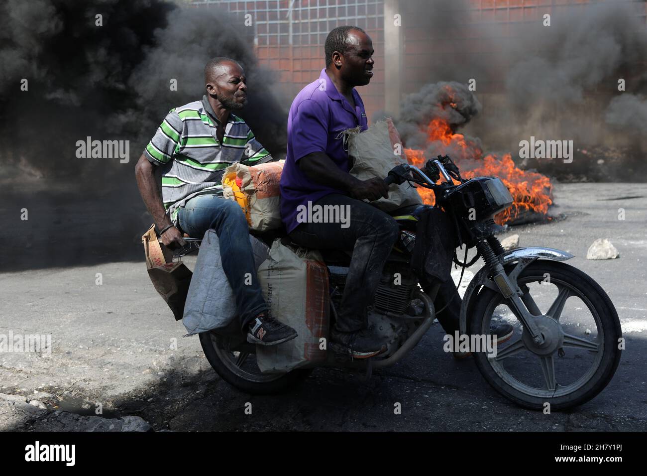Two men on a motorcylce ride past a burning street baricade during demonstrations against widespread kidnappings, in Port-au-Prince, Haiti November 25, 2021. REUTERS/Ralph Tedy Erol Stock Photo