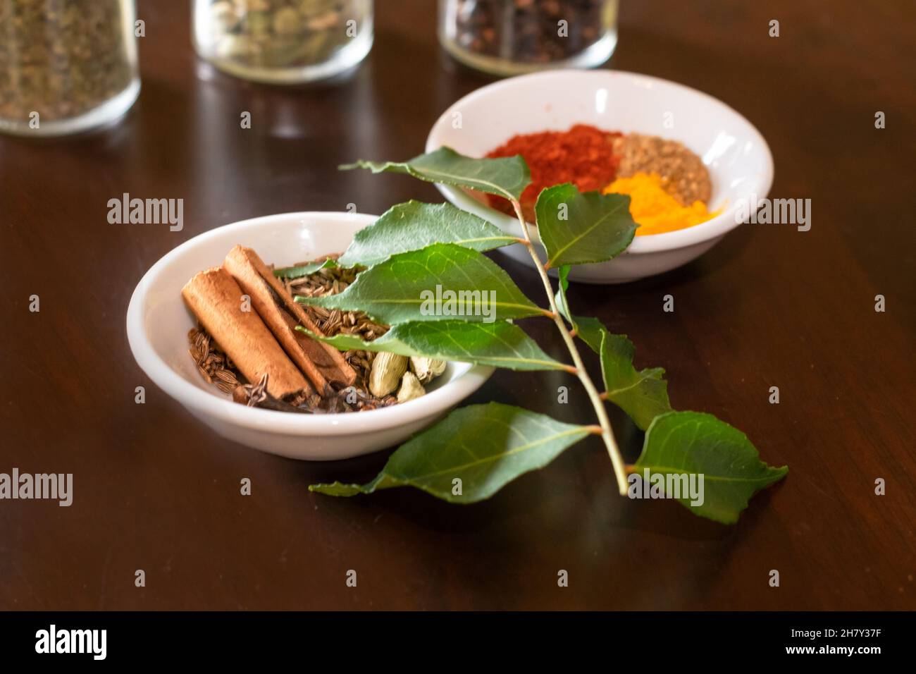 Mixture of Asian spices used to make curry displayed on a wooden table with fresh curry leaves as a garnish Stock Photo