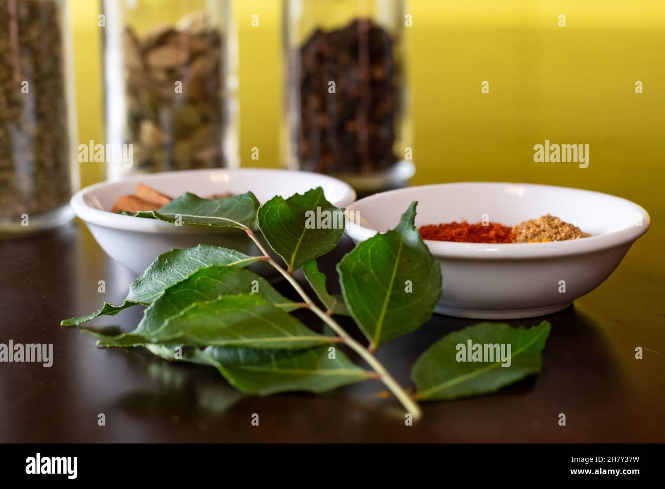 Mixture of Asian spices used to make curry displayed on a wooden table with fresh curry leaves as a garnish Stock Photo