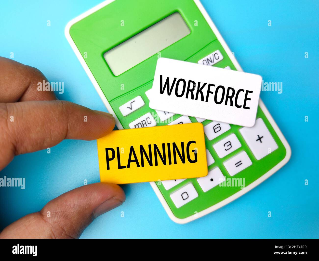 Calculator and hand holding colored wooden board with the word WORKFORCE PLANNING. Stock Photo