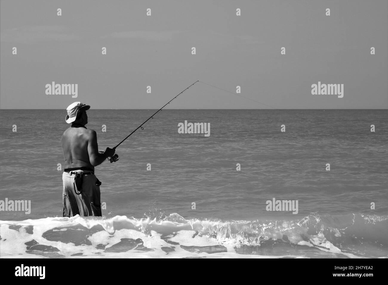 Man with hat fishing in ocean Stock Photo