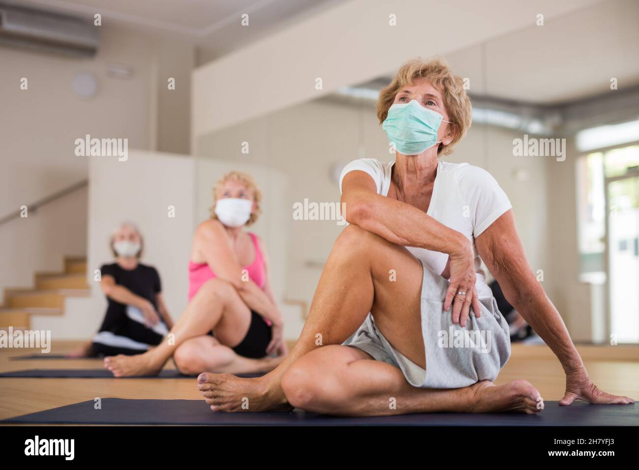 Elderly woman in protective mask doing yoga during group training Stock Photo