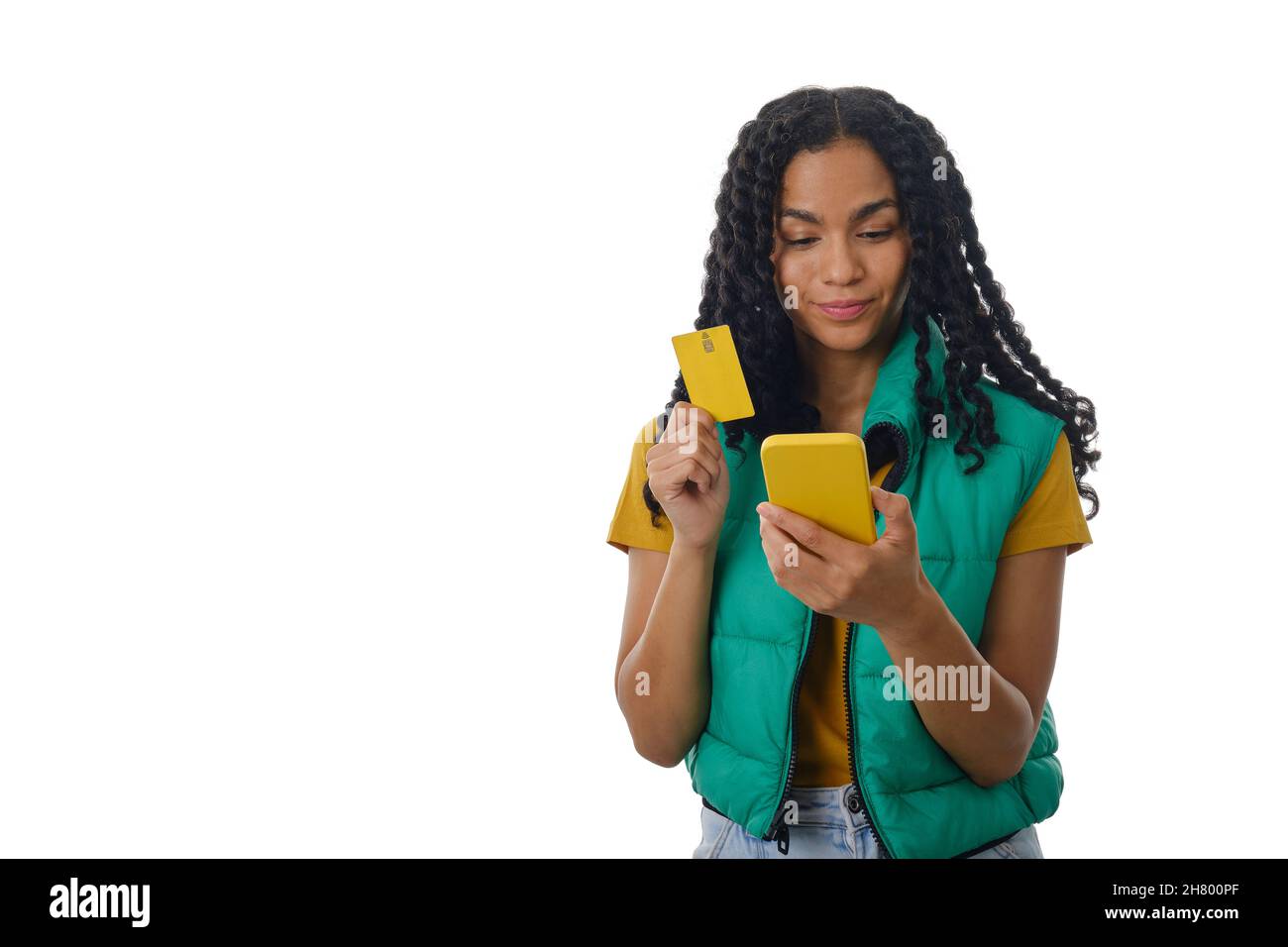 Latin woman holding a mobile phone and a credit card while standing over an isolated background. Stock Photo