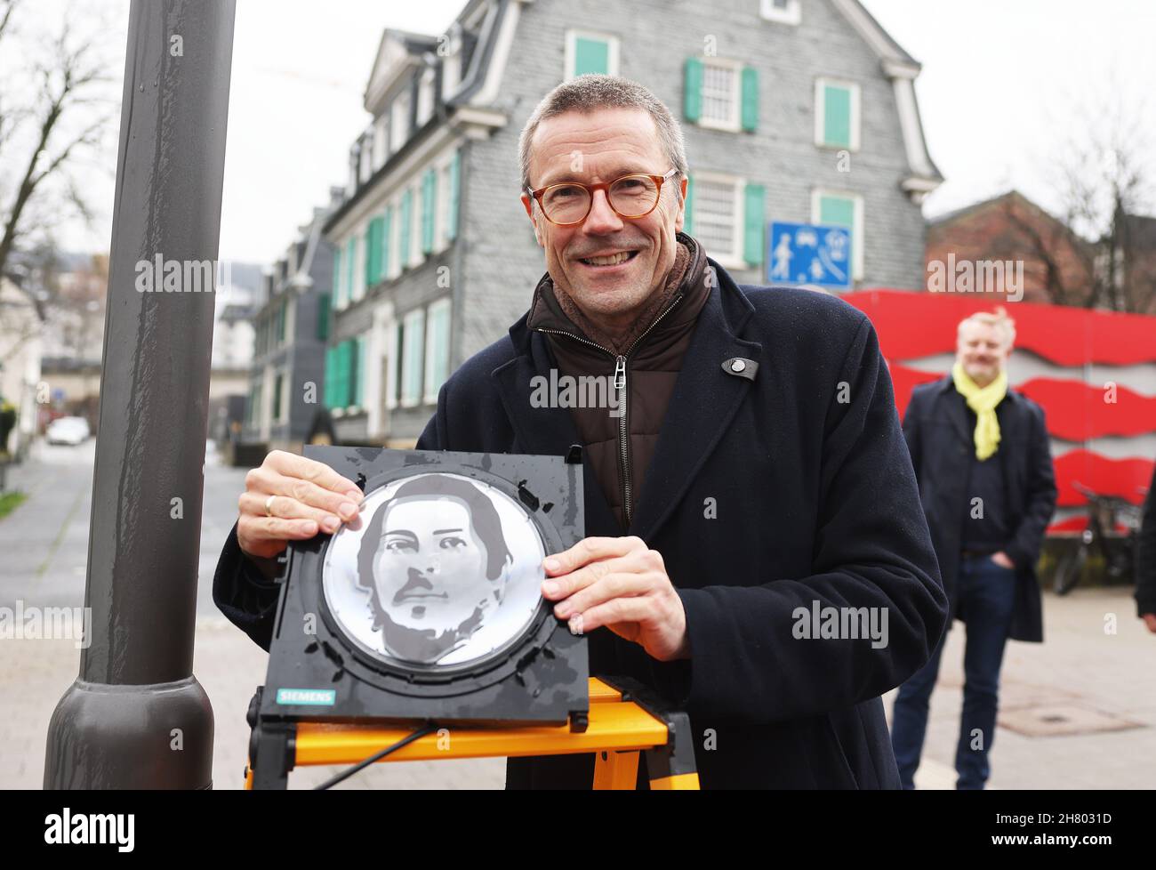 Wuppertal, Germany. 26th Nov, 2021. Uwe Schneidewind (Greens), Lord Mayor of Wuppertal, shows a traffic light man with the face of Friedrich Engels. On the occasion of the Engels Year, the city has installed the traffic light manikin opposite the Engels House at a pedestrian crossing. Friedrich Engels (1820-1895) was born in the Wuppertal district of Barmen and wrote 'The Manifesto of the Communist Party' together with Marx. Credit: Oliver Berg/dpa/Alamy Live News Stock Photo