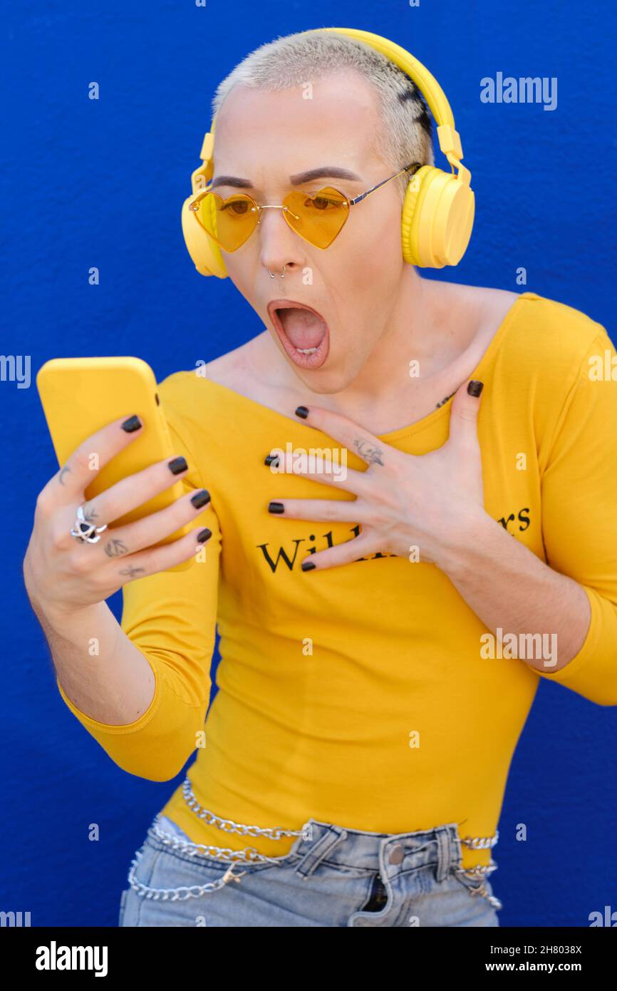 Non-binary young person looking shocked and speechless while checking mobile phone. Stock Photo