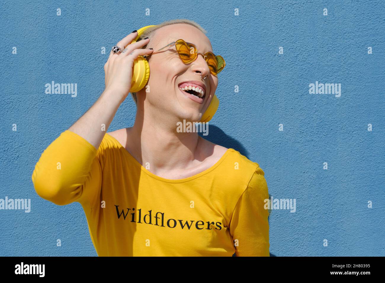 Happy young non-binary smiling while enjoying listening music with headphones outdoors. Stock Photo