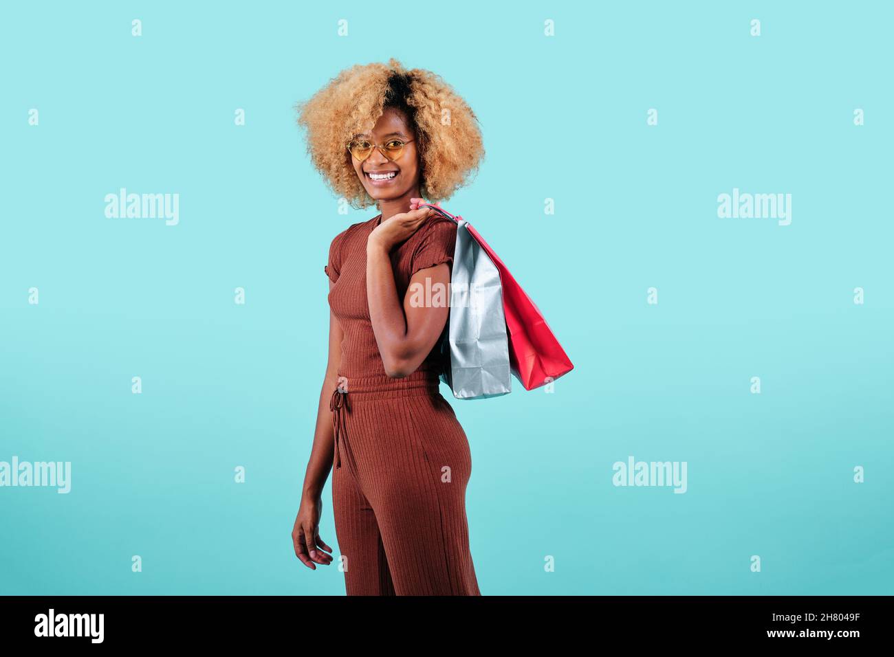 Smiling afro woman carrying colorful shopping paper bags over an isolated background. Black Friday sales concept. Stock Photo