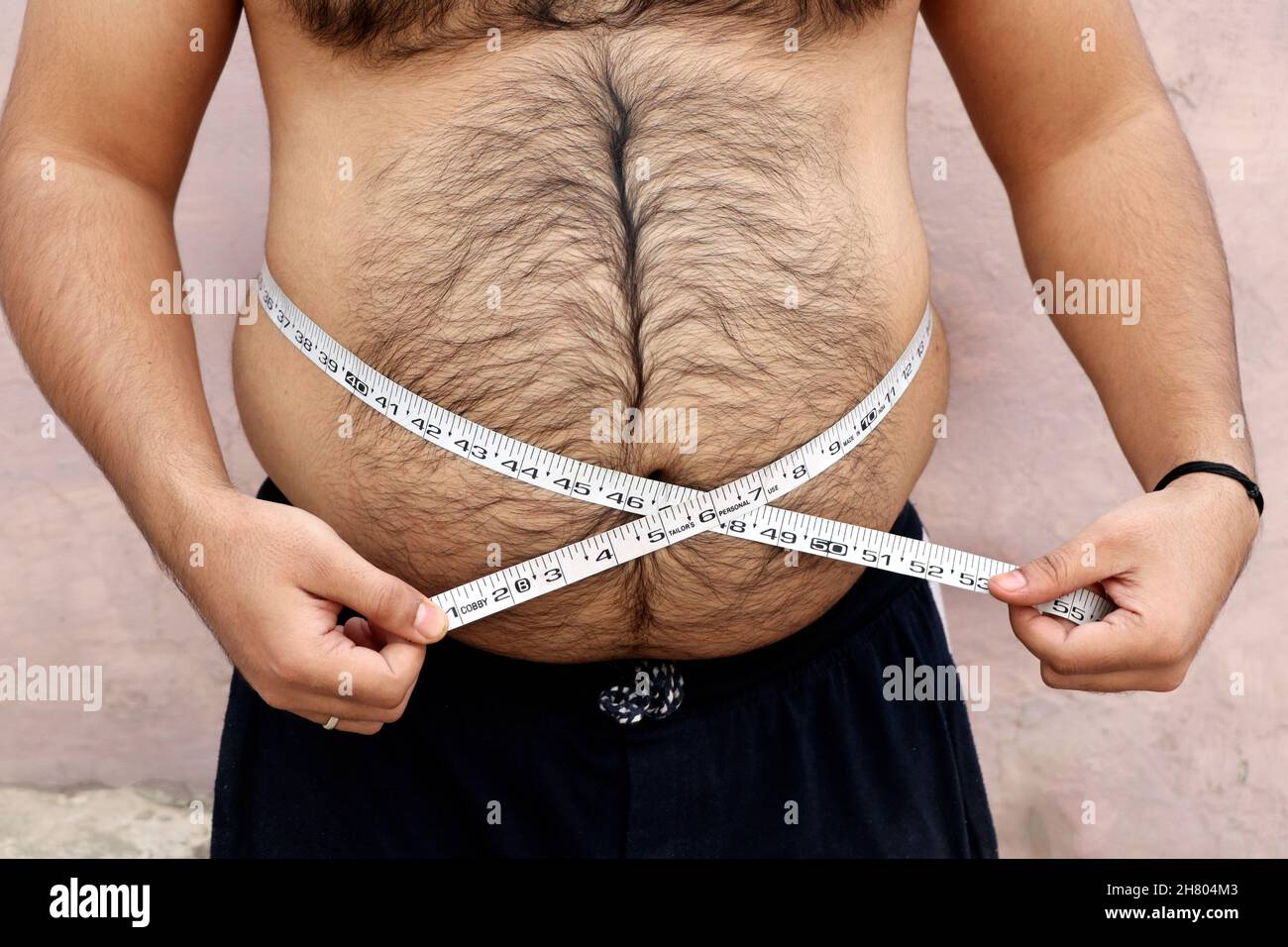 A asian men measures his fat belly with a measuring tape on a plain background Stock Photo
