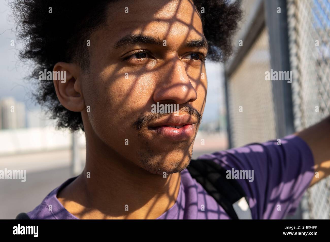 African American male with Afro curls and shadow from metal net looking away with thoughtful glance Stock Photo