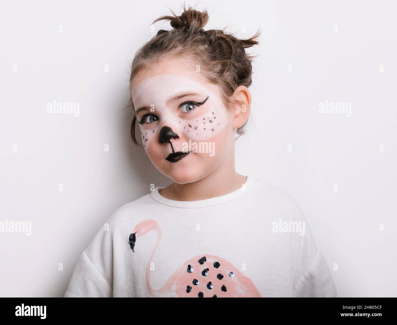 Adorable girl with cat face paint in t shirt looking at camera on white background in light