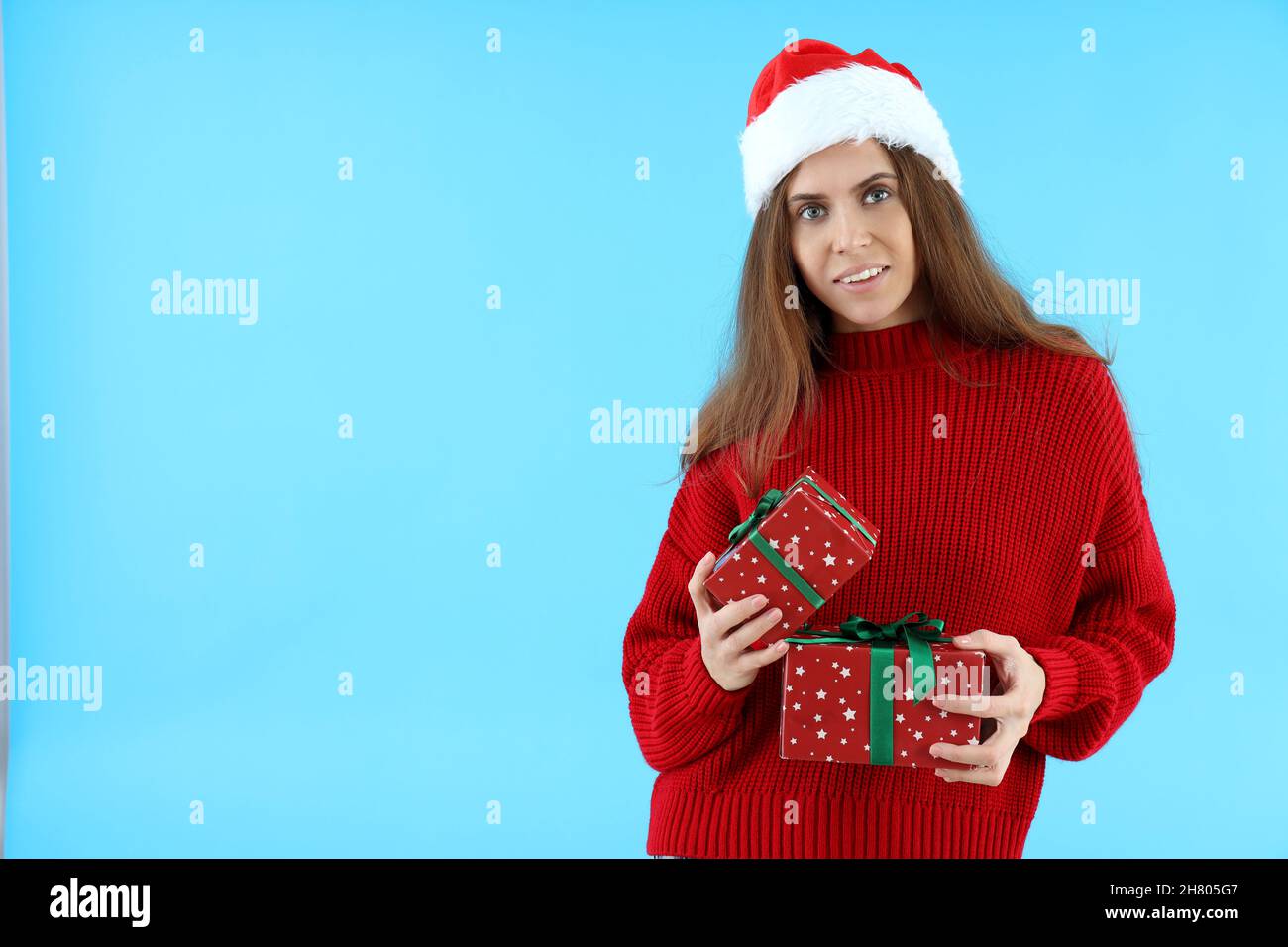 Attractive woman in Santa hat holds gift boxes on blue background Stock ...