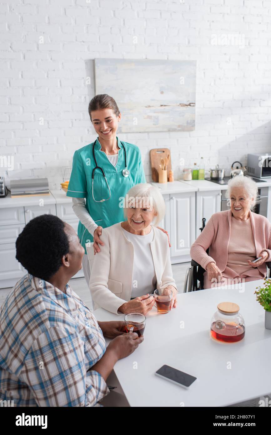 Smiling nurse standing near multiethnic patients with smartphones and