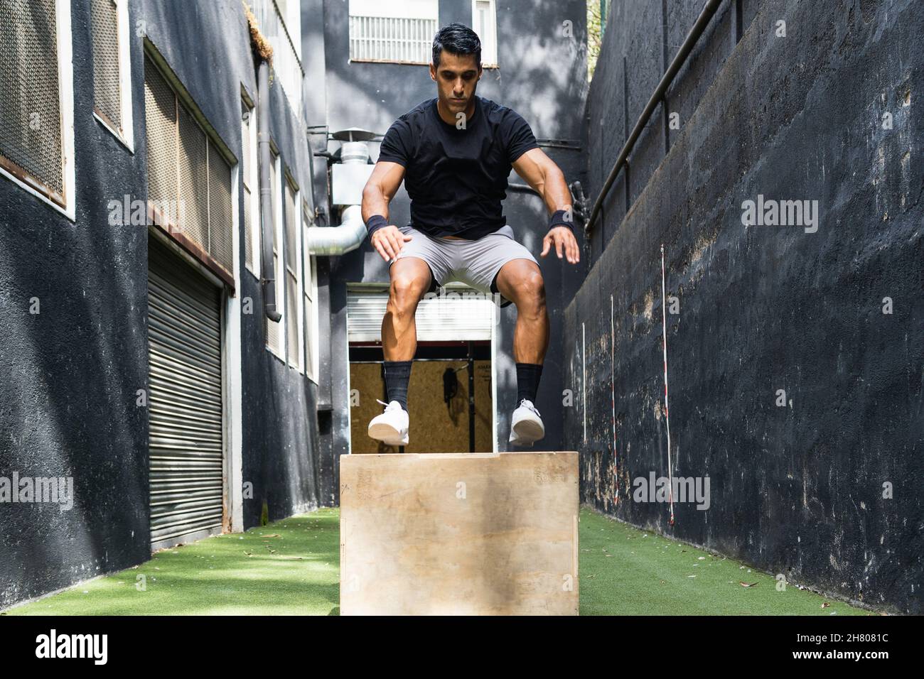 Full body of serious Hispanic male in sportswear jumping on wooden box
