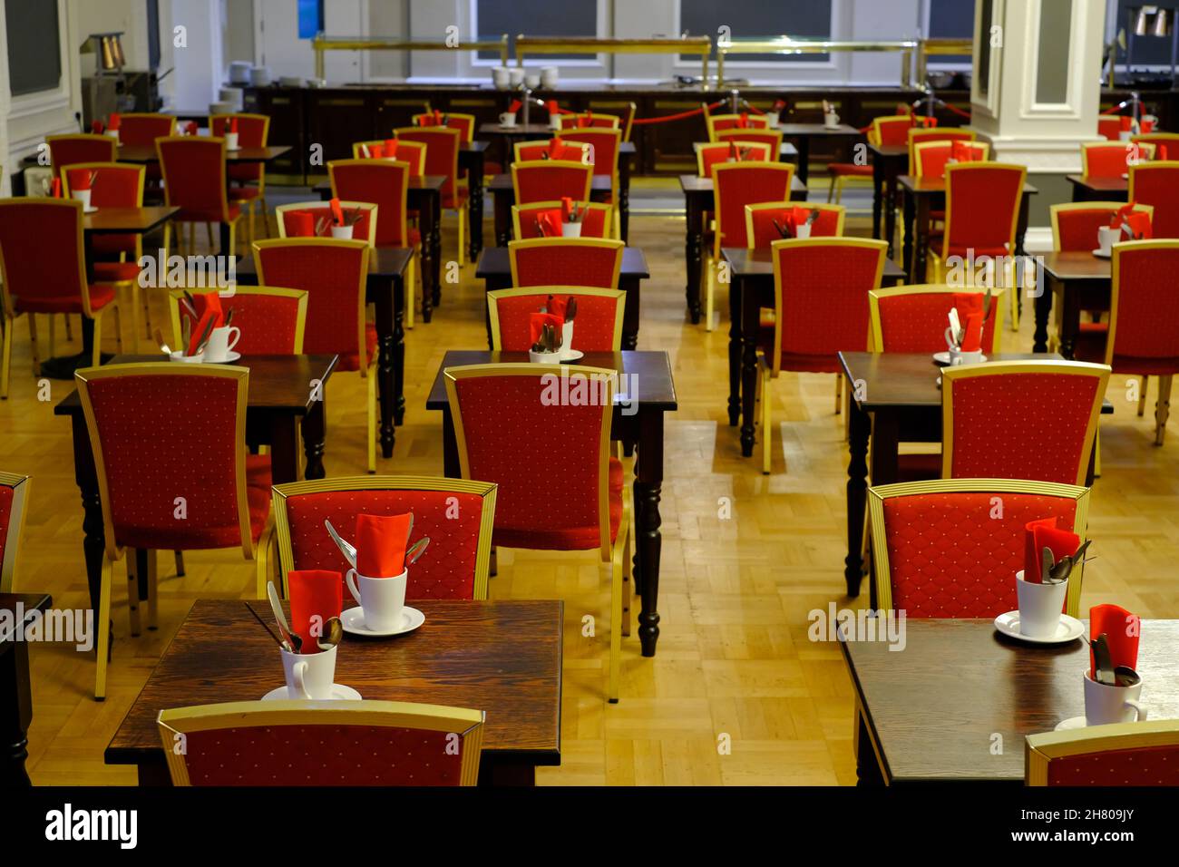 Regimented rows of tables and red chairs in a large hotel dining room
