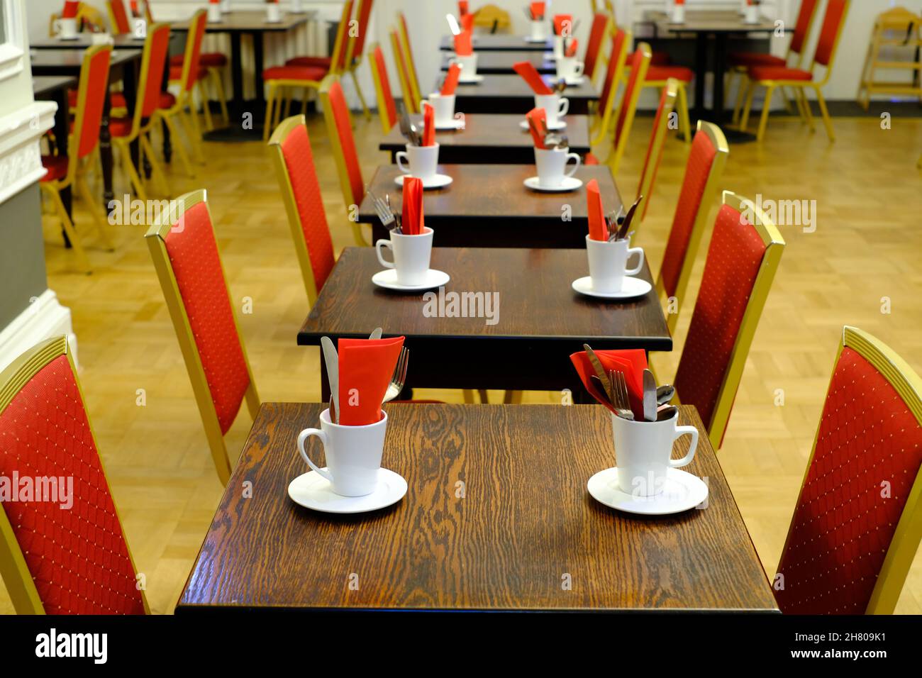 Regimented rows of tables and red chairs in a large hotel dining room suggest formality rather than relaxed comfort. Stock Photo