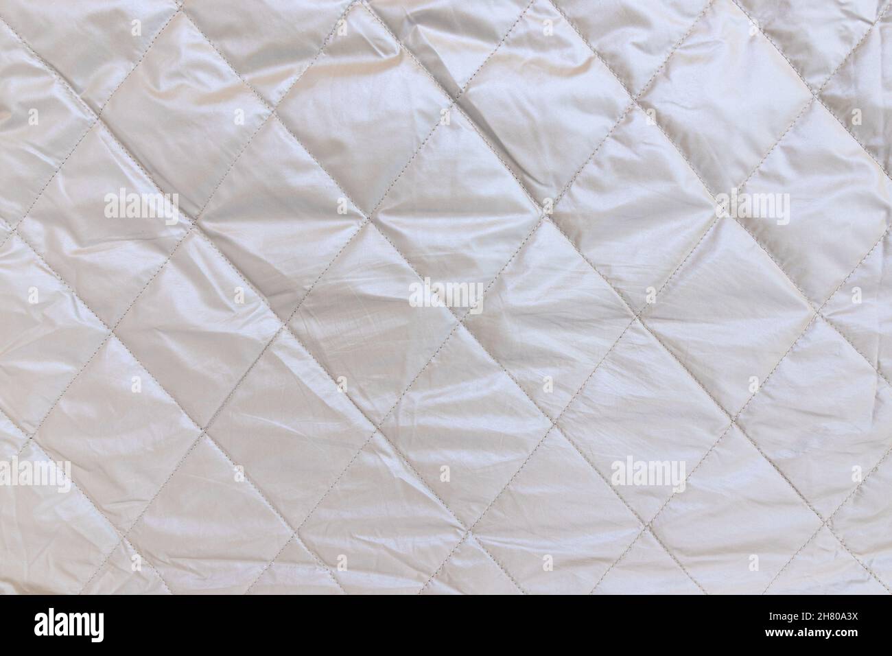 square stitched on silver grey cloak, seamless background pattern and texture, silver background of reflectiv quilted fabric, close up Stock Photo