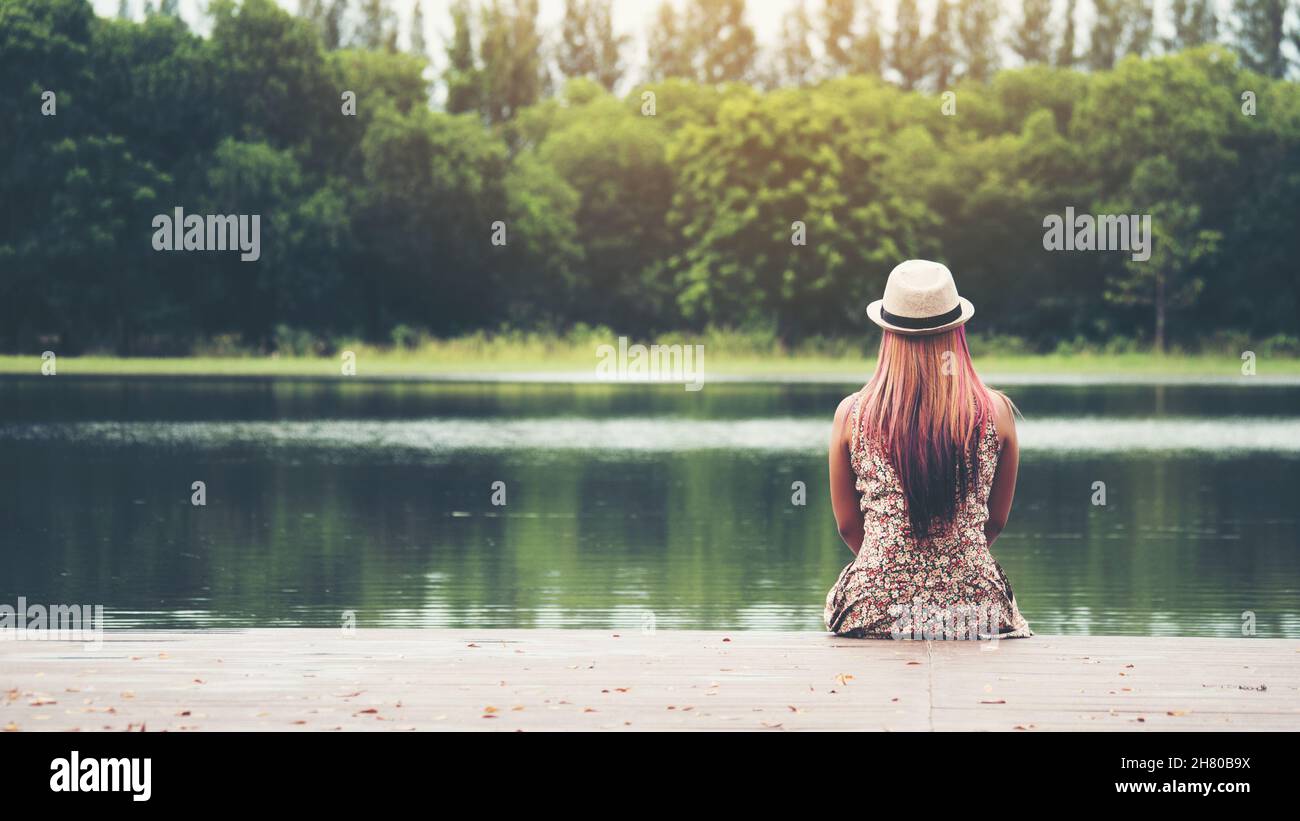 Young woman sitting on pier and looking at the river Stock Photo - Alamy