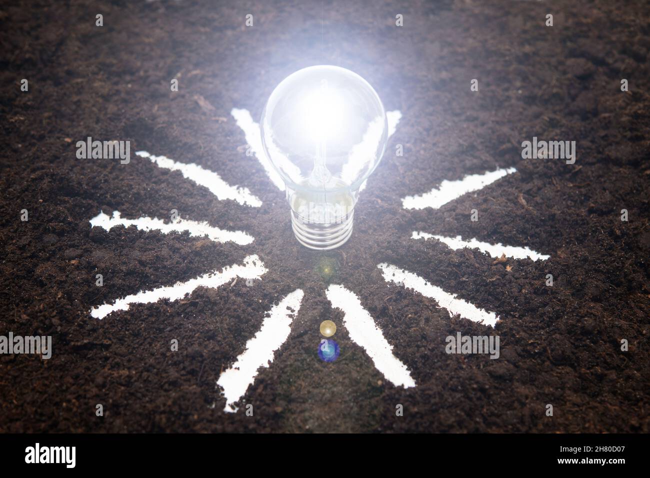 Glowing light bulb with a sun symbol on the soil. Solar power concept. Stock Photo