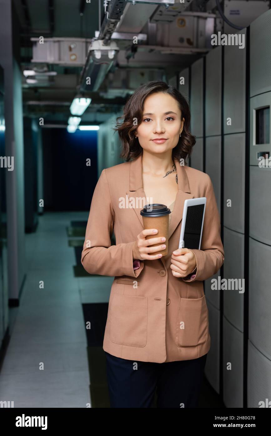 young engineer with paper cup and digital tablet looking at camera in data center Stock Photo