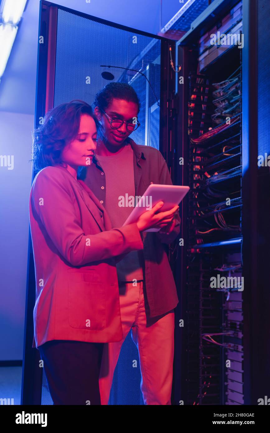 interracial engineers using digital tablet while checking server in data center Stock Photo