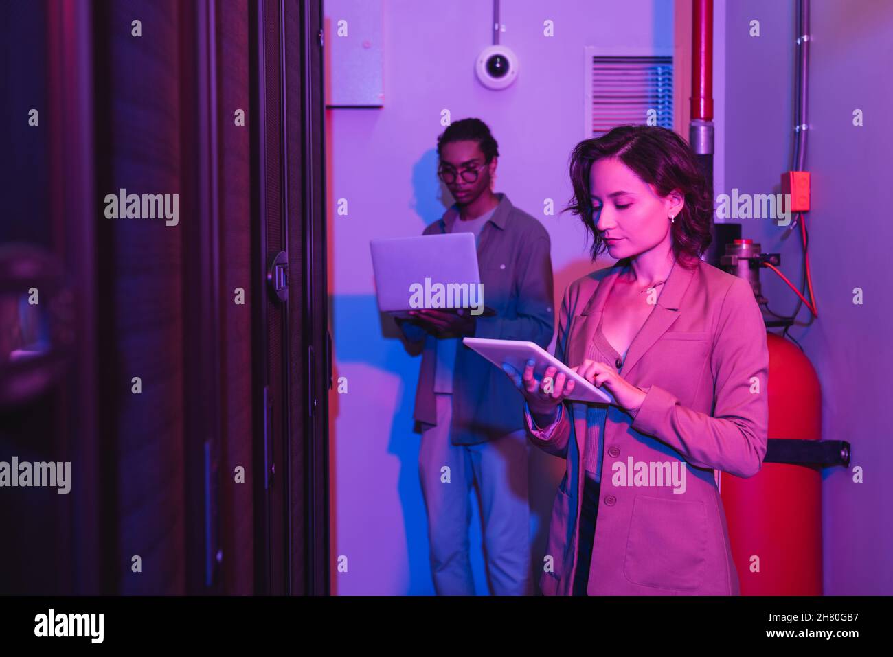 interracial programmers using gadgets while working in data center in neon light Stock Photo