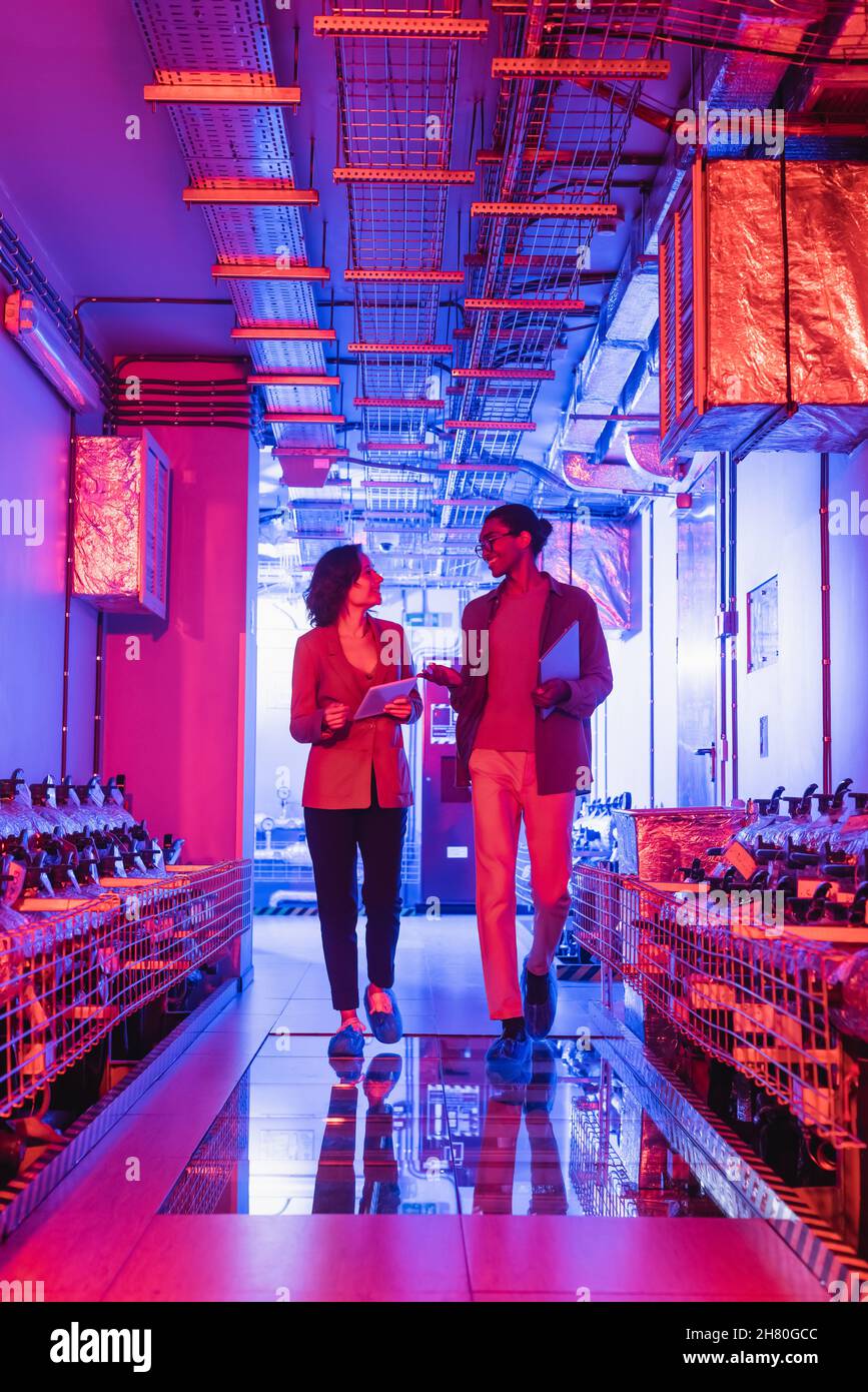 multiethnic engineers with gadgets talking while walking in technical equipment room in data center Stock Photo