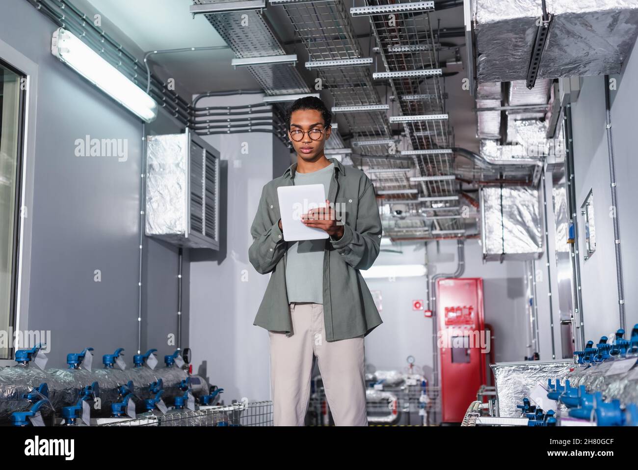 young afican american engineer using digital tablet while standing near cooling system  of data center Stock Photo