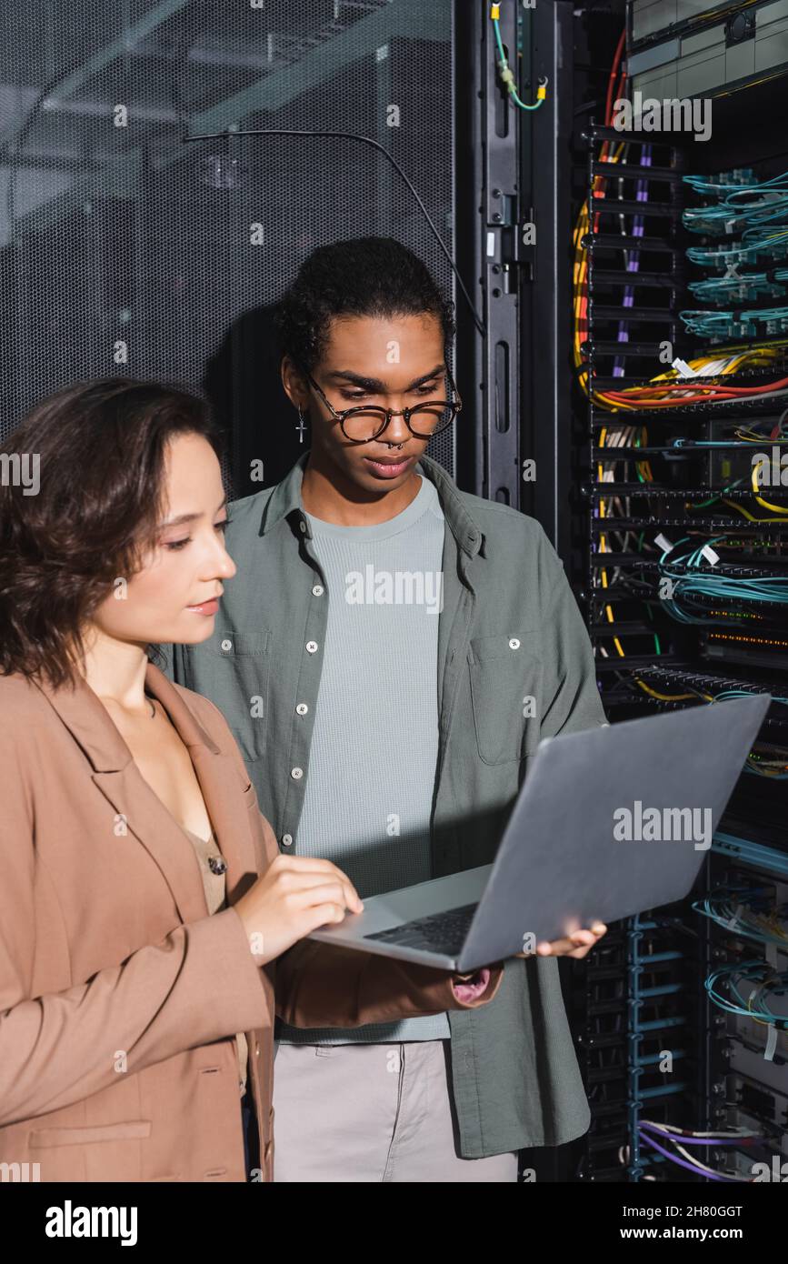 multiethnic technicians working on laptop near server in data center Stock Photo