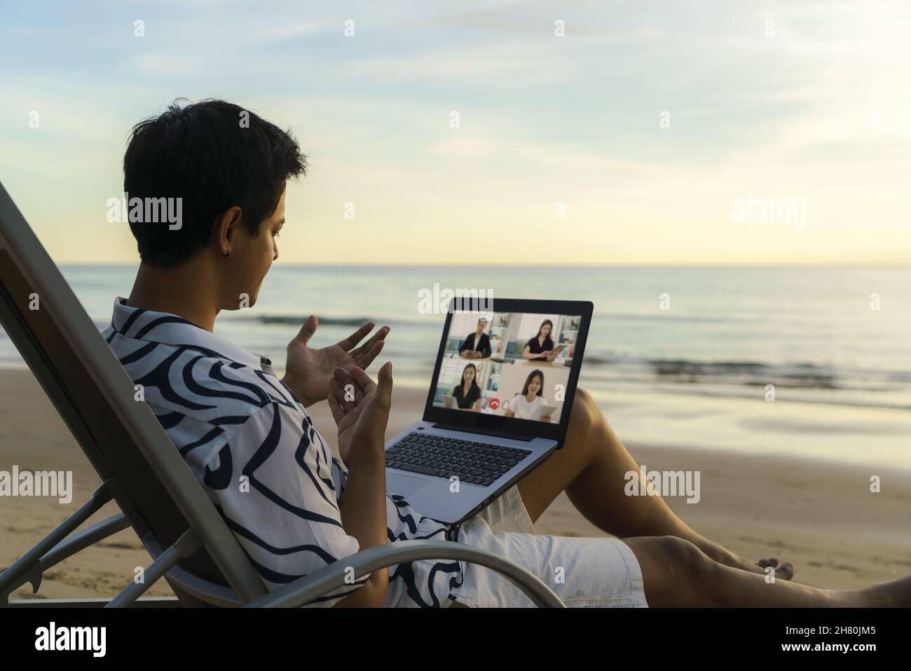 Asian business man having remote video conference call with his business team at the beach during vacation in holiday. Stock Photo