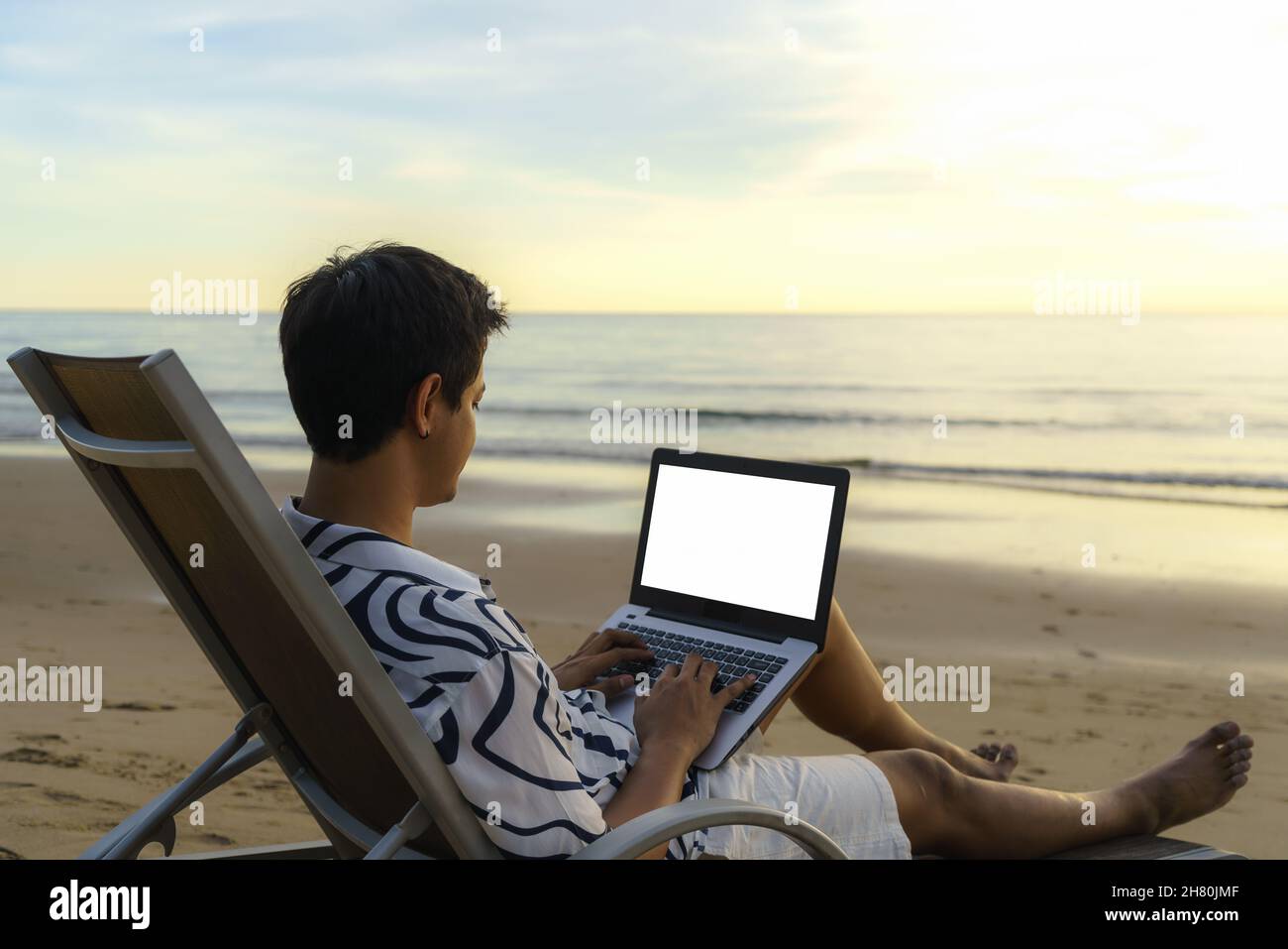 Lifestyle of young Asian man blogger working and using keyboard on laptop while sitting on the beautiful beach, freelance travel on holiday summer dur Stock Photo