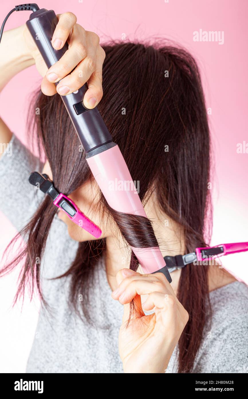 A beautiful young caucasian woman is using a conical electrical curler wand or curling iron to create curles in her red brown hair. DIY cosmetics conc Stock Photo