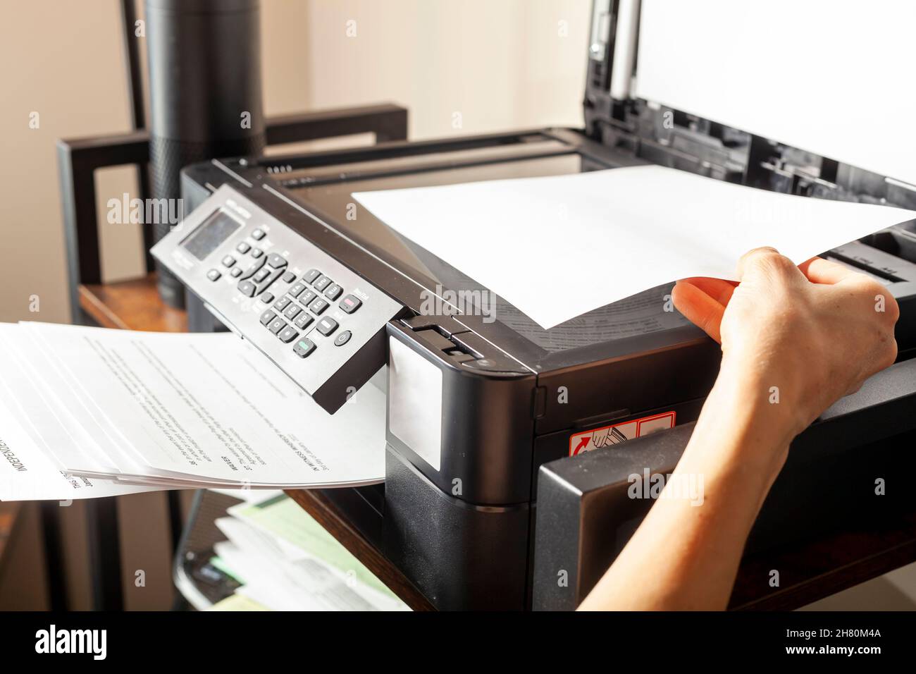 Concept image for office work. A woman is placing or removing paper. There is a wireless photocopier, scanner, printer combo device on top of a shelvi Stock Photo