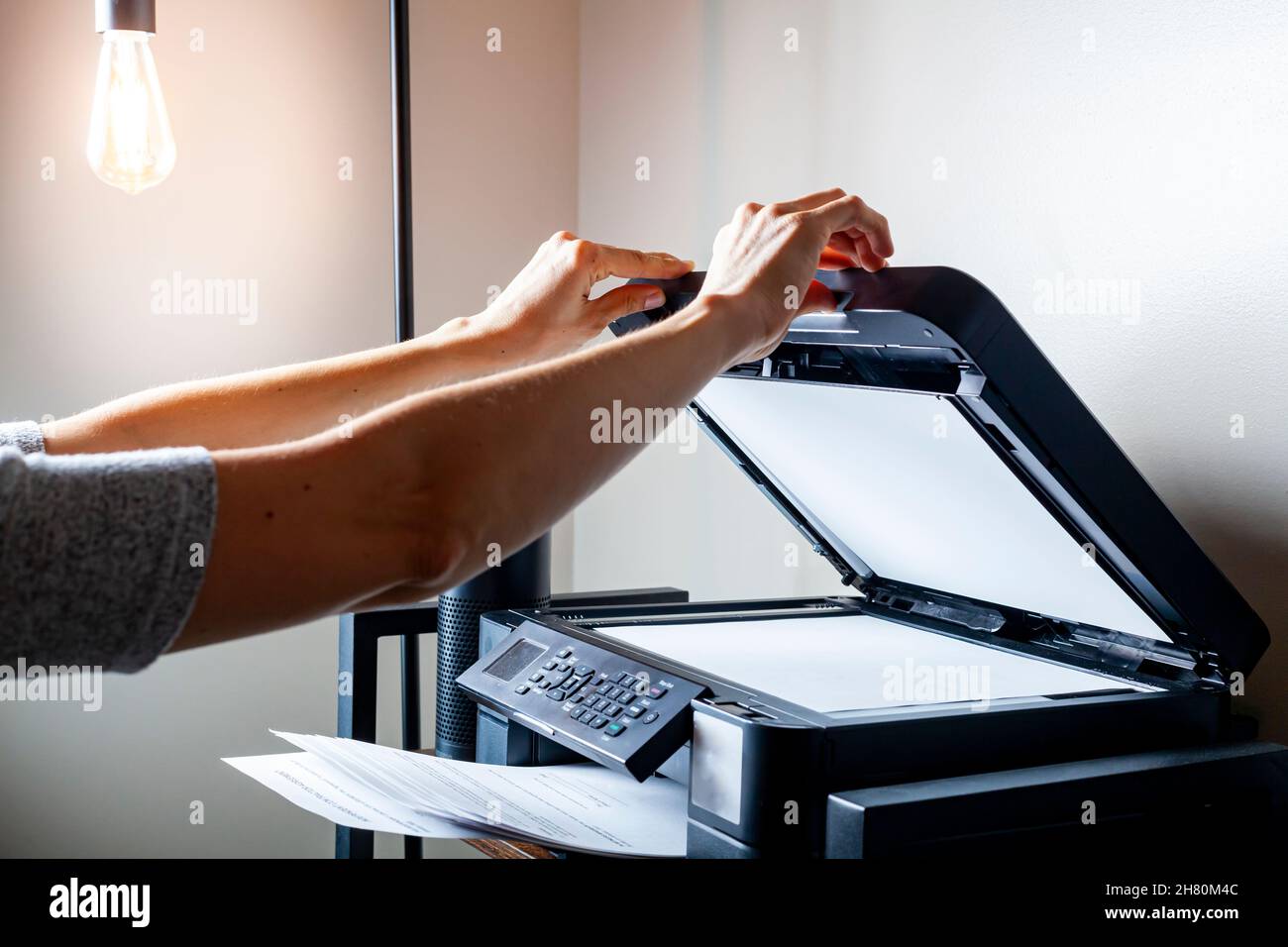 Concept image for office work. A woman is placing or removing paper. There is a wireless photocopier, scanner, printer combo device on top of a shelvi Stock Photo