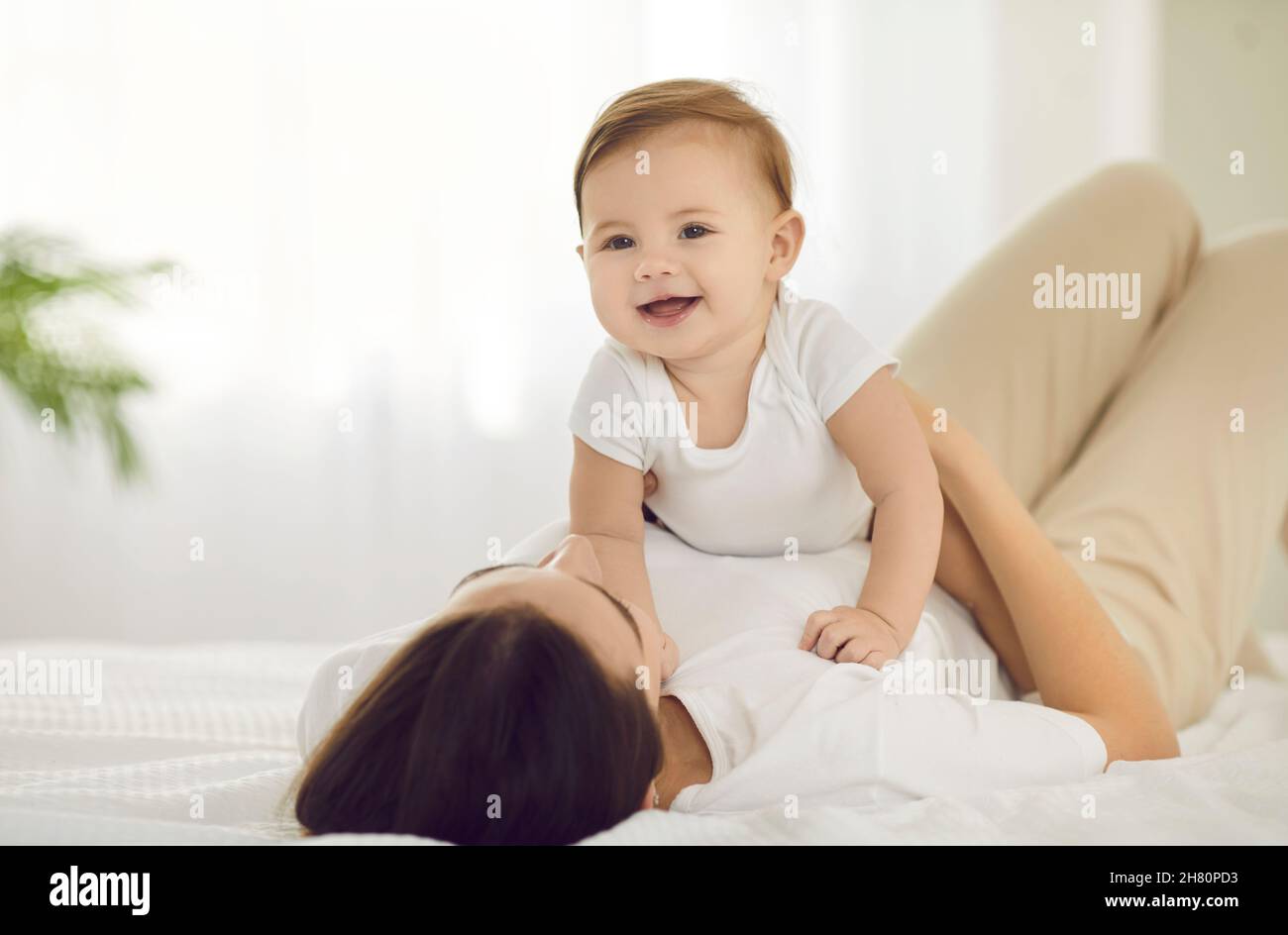 Little baby girl and her mom in morning having fun together playing on white bed. Stock Photo