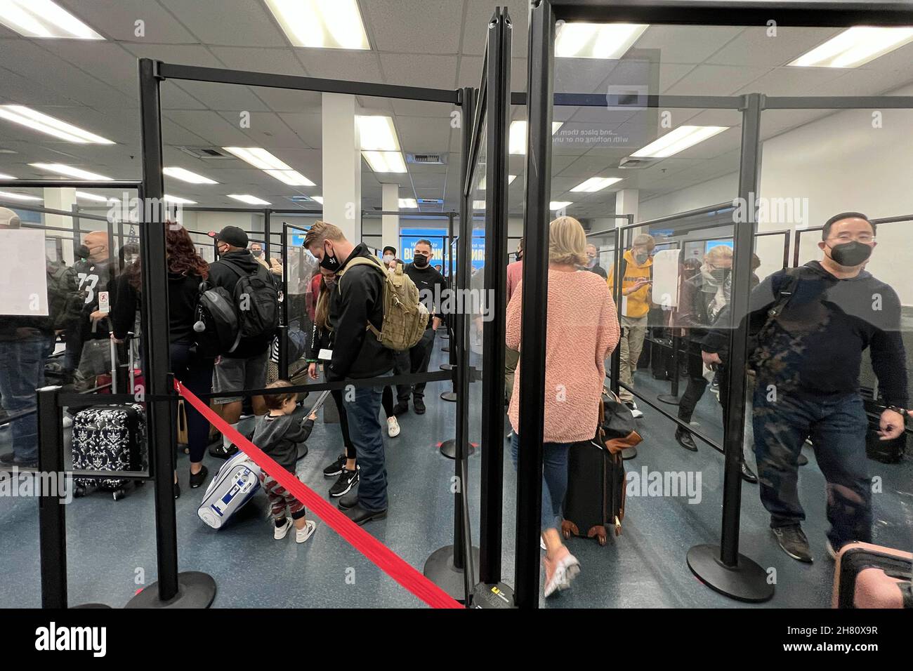 Passengers wearing face masks stand in line behind plexiglass barriers
