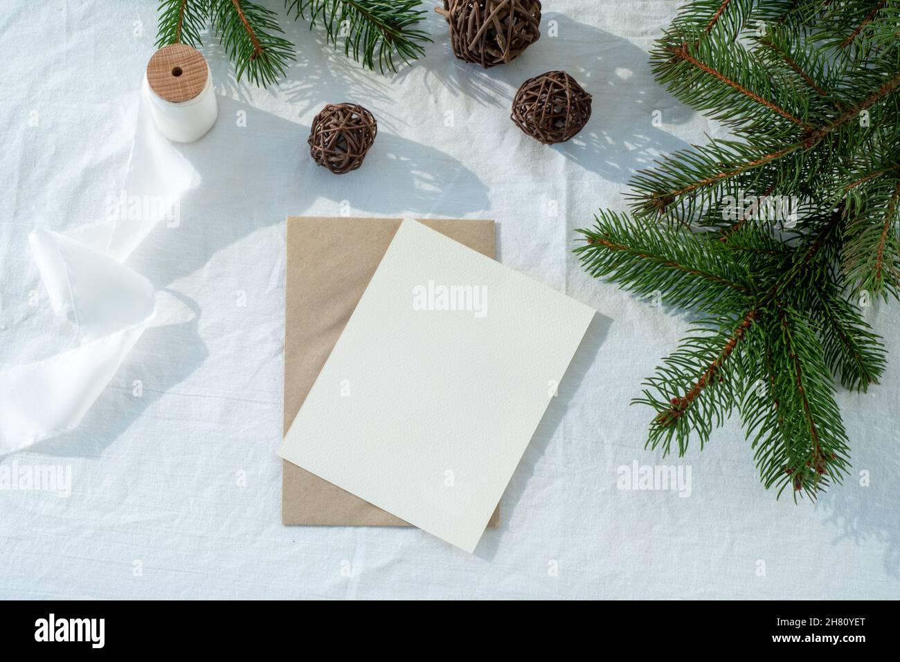 Blank greeting card, invitation card mockup.Christmas decoration scene with card and envelope, ribbon, fir branches and wooden balls.White linen backg Stock Photo