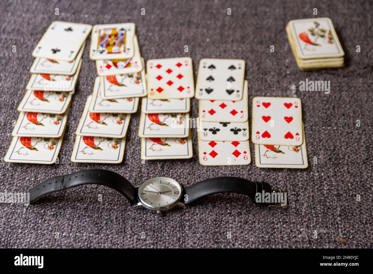A wrist watch in front of a game of solitaire or pateince implying killing time, wasting time etc. Stock Photo