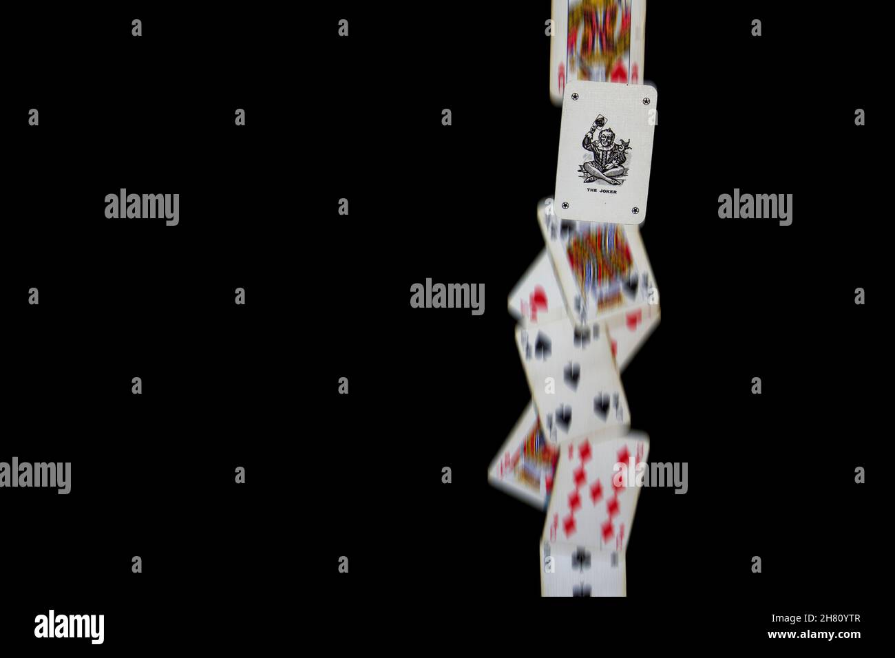 A line of playing cards fall against a black background, with the joker frozen to show it is different to the other cards. Landscape orientation. Stock Photo