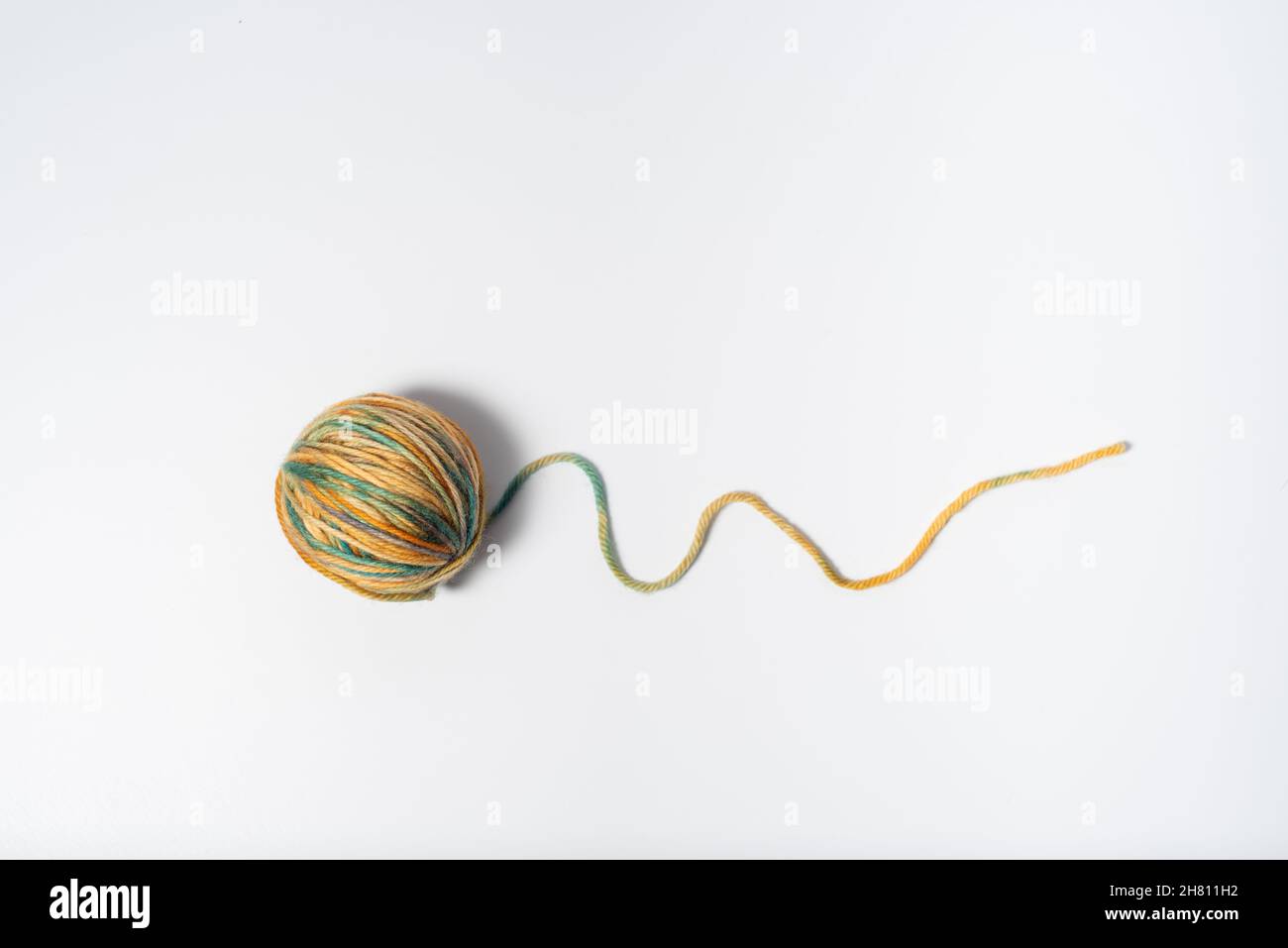 Small ball of light multicolored yarn with a loose string on white ...