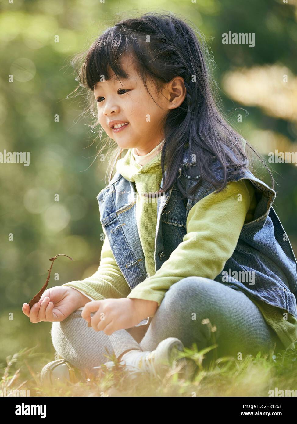 outdoor portrait of an asian little girl sitting on grass happy and smiling Stock Photo