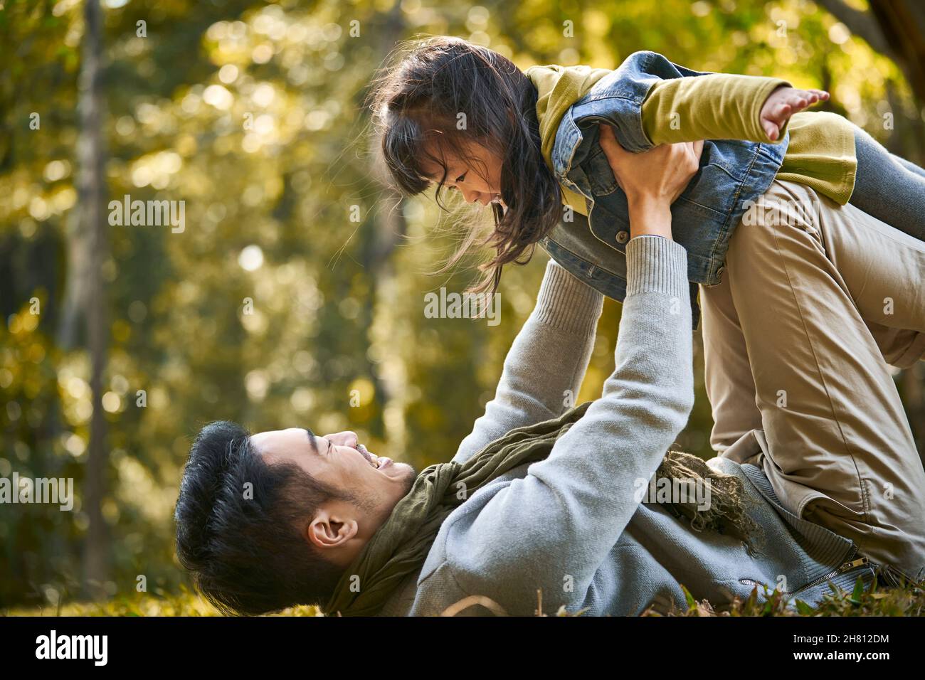asian father and daughter having fun outdoors on the grass in city park Stock Photo