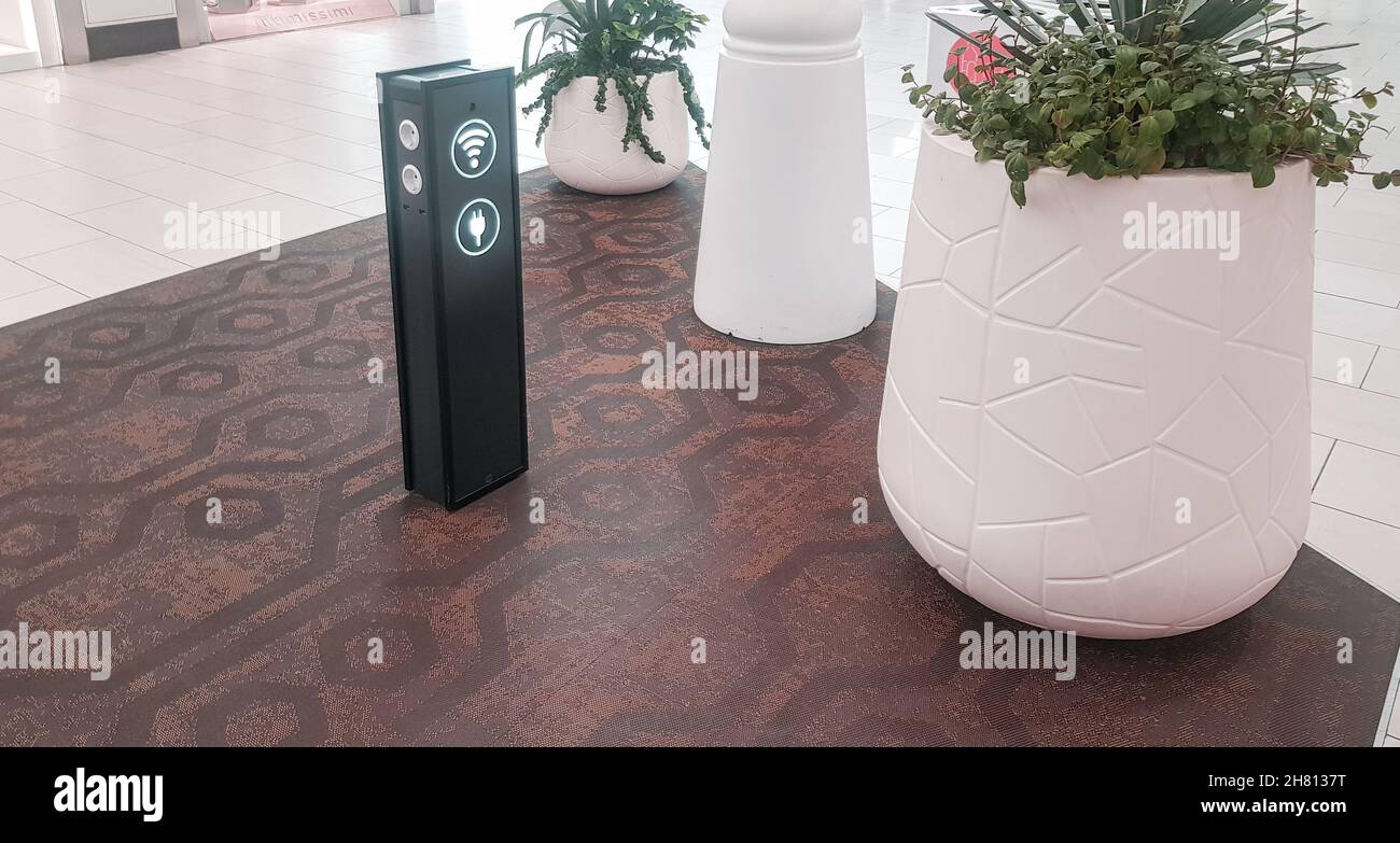 Wi-Fi zone with a rack for charging gadgets via usb and at the airport or supermarket, nearby plants in white flower pots. Stock Photo