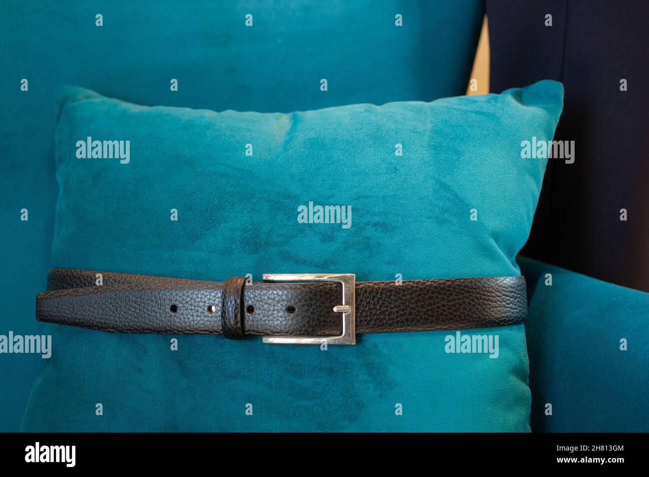 A man genuine leather black belt, classic metal buckle tied to a green pillow Stock Photo