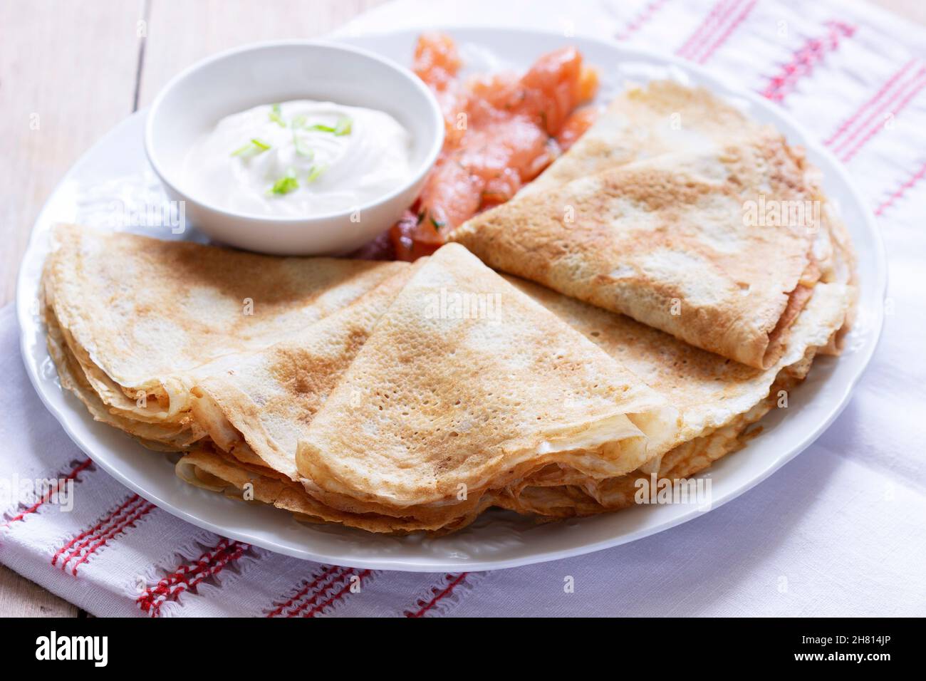 Thin pancakes with salmon and sour cream on a light background. Rustic style. Stock Photo