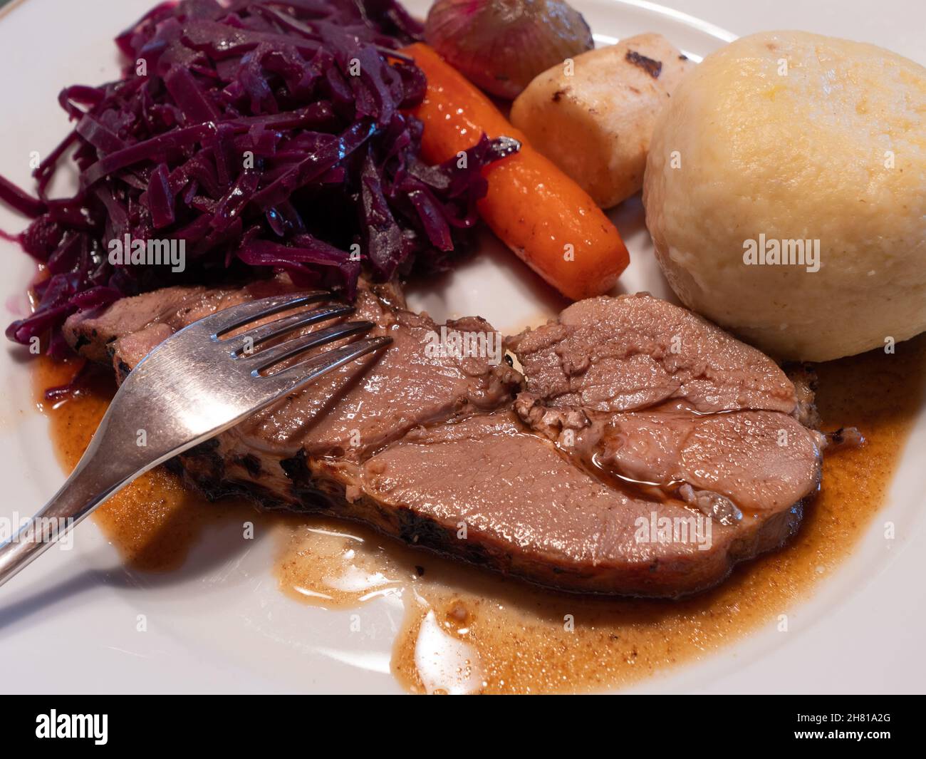 Slice of Roast Young Wild Boar Piglet with Red Cabbage, Potato Dumpling, Winter Vegetables and Gravy Stock Photo