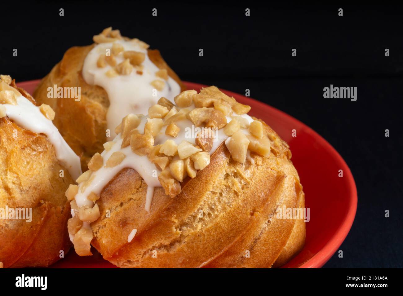 Round eclair in a red plate on the table. Food on a black background Stock Photo