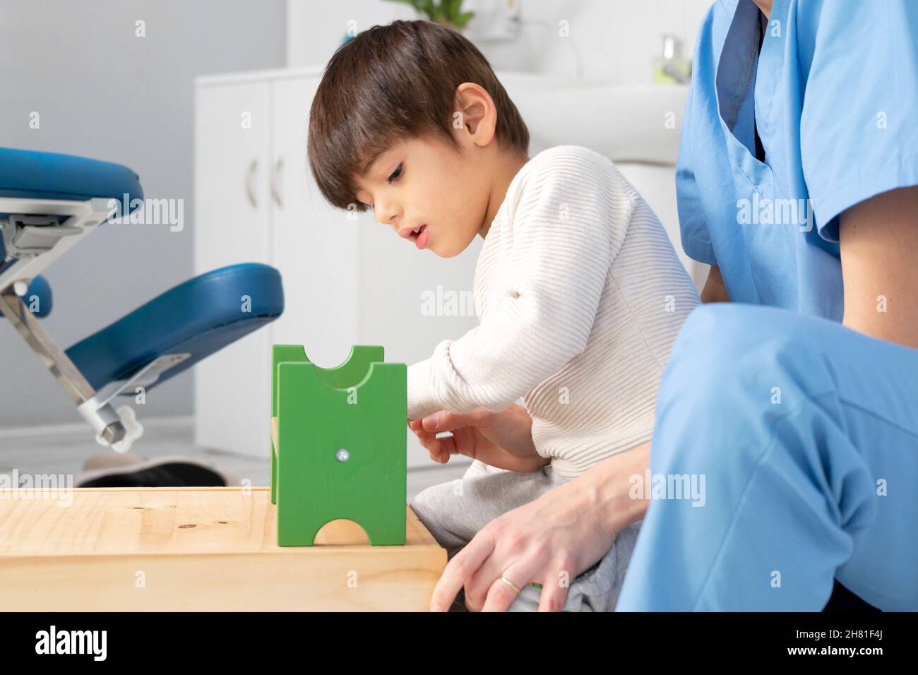 cute kid with disability playing with developing toys while is being helped by physiotherapist in rehabilitation hospital. High quality photo Stock Photo